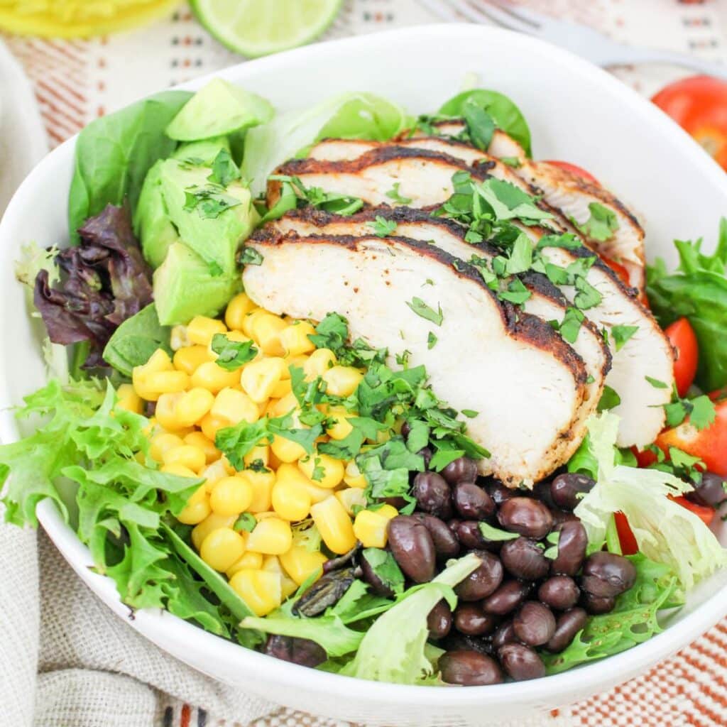 Chicken, mixed greens, black beans, corn, diced avocado, cherry tomatoes, and chopped cilantro in a large salad bowl