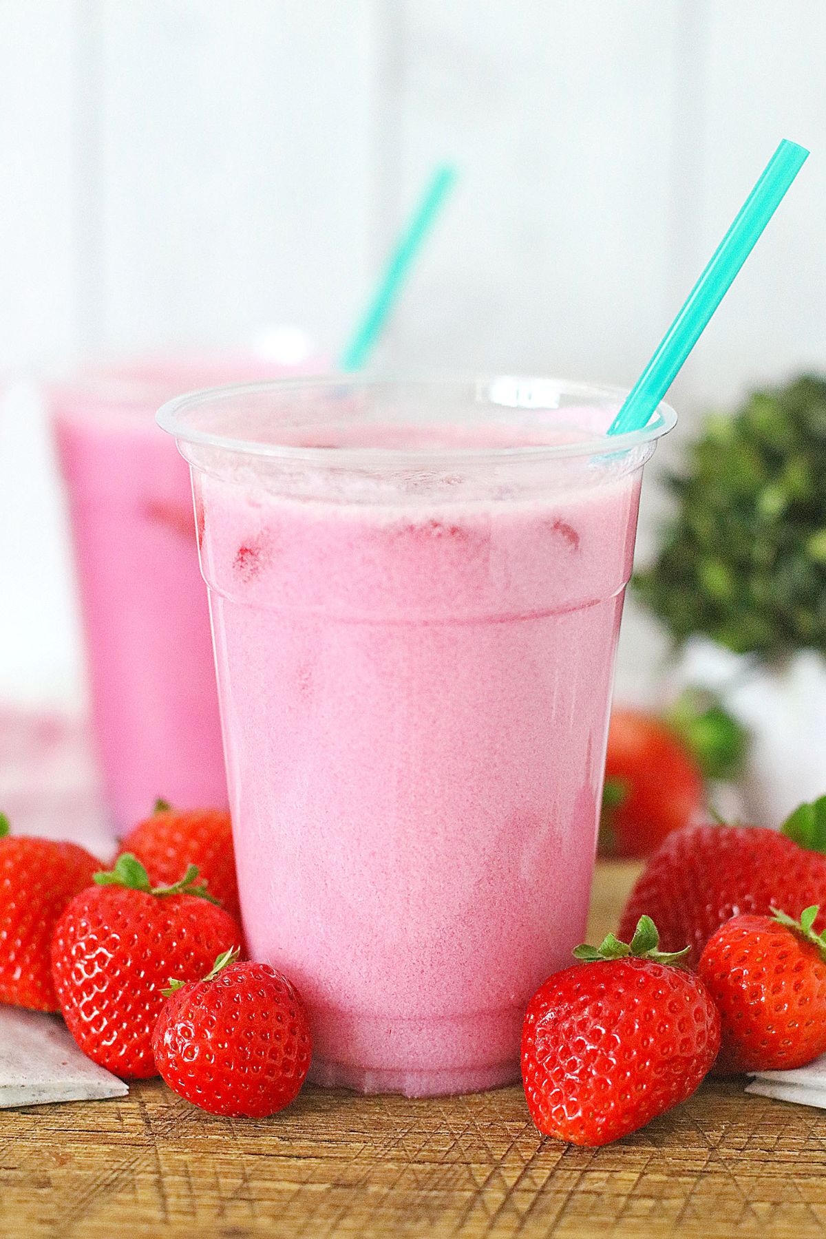 Starbucks pink drink in a clear cup with a blue straw and strawberries around the cup.