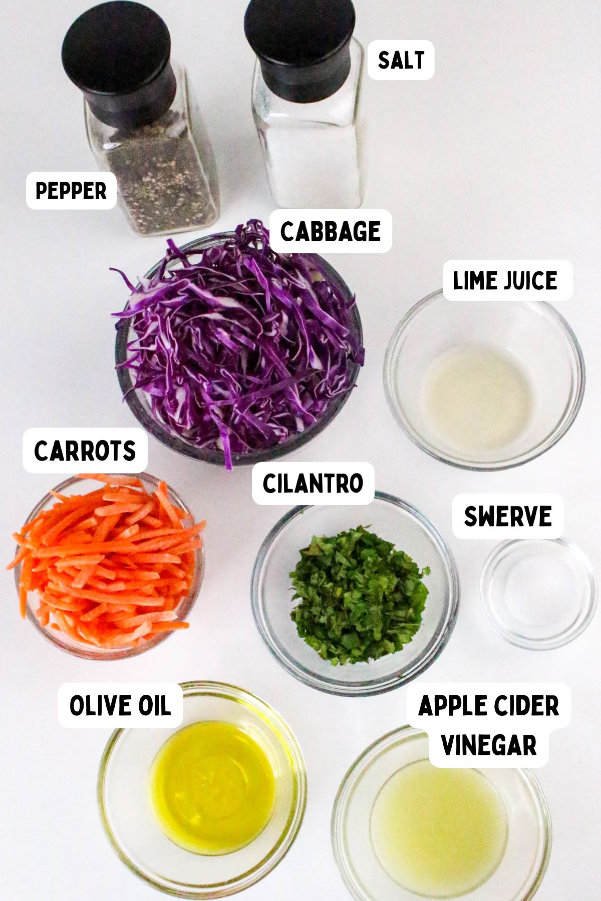 A top-down view of bowls and containers holding shredded cabbage, sliced carrots, chopped cilantro, olive oil, apple cider vinegar, lime juice, Swerve sweetener, salt, and pepper, all labeled.