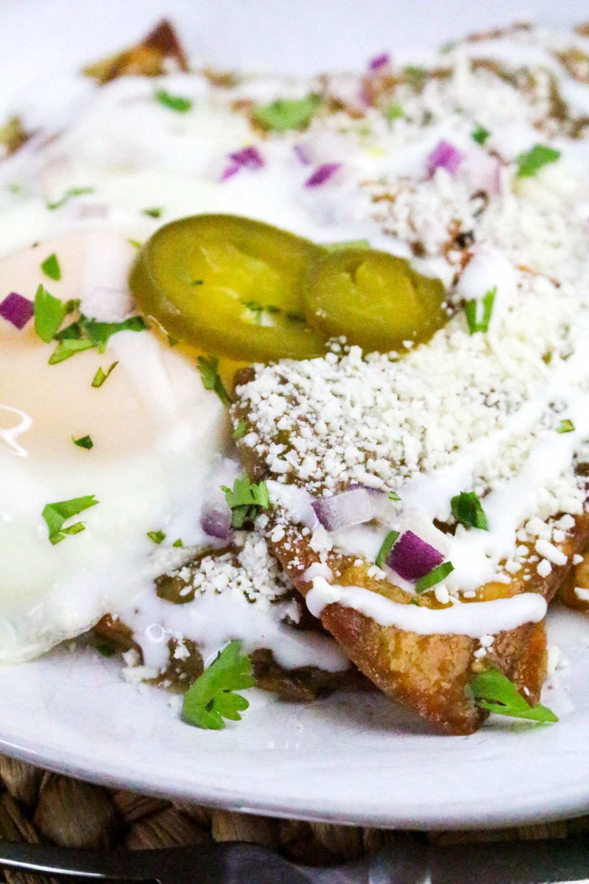 A plate of chilaquiles topped with fried eggs, crumbled cheese, sliced jalapeños, chopped red onions, cilantro, and a drizzle of crema.