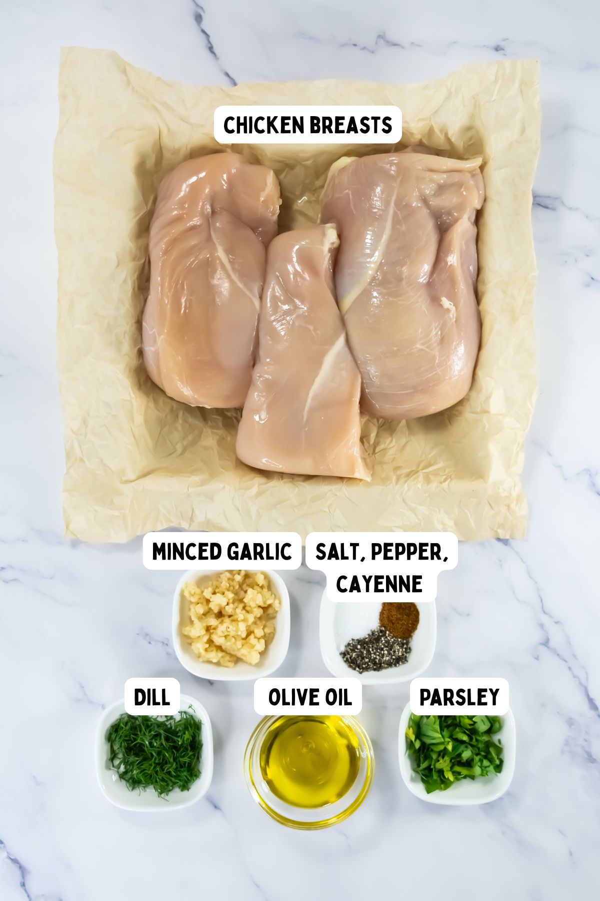 Three raw chicken breasts are on parchment paper. Surrounding them are small bowls containing minced garlic, a mix of salt, pepper, and cayenne, chopped dill, olive oil, and chopped parsley, all labeled.
