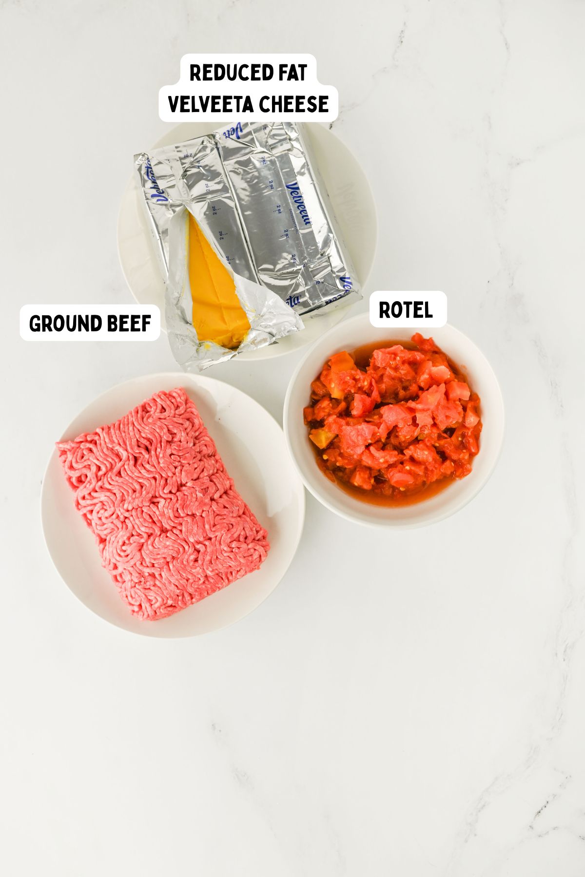 A plate of raw ground beef, a bowl of diced tomatoes with green chilies labeled “Rotel,” and a partially unwrapped block of reduced fat Velveeta cheese on a white surface.