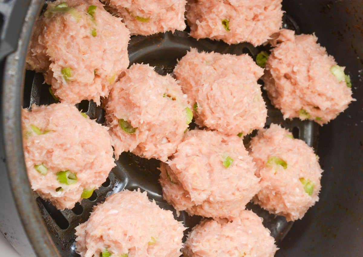 Raw, uncooked meatballs with visible green chopped pieces, possibly vegetables or herbs, are arranged in a circular pattern inside the basket of an air fryer or similar cooking appliance.