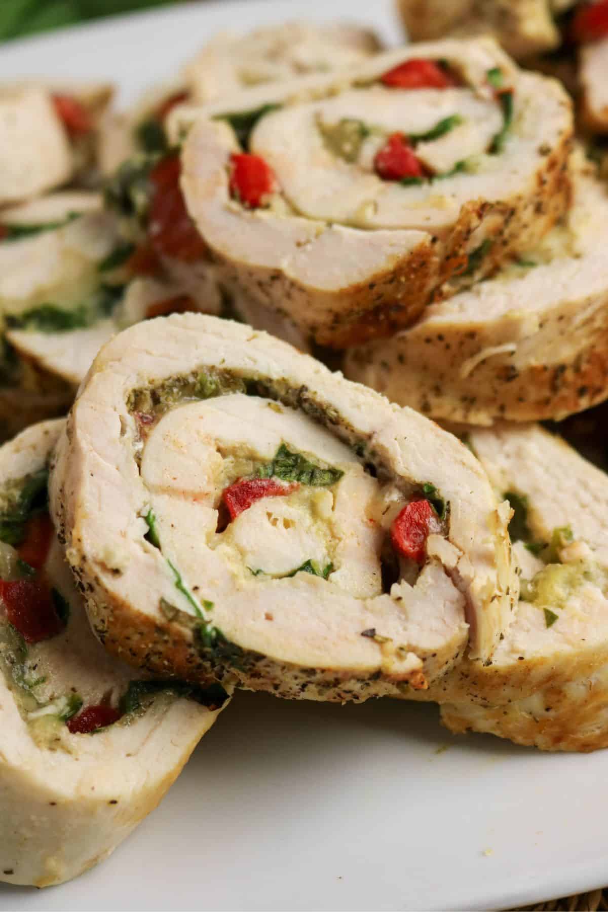 Sliced rolled chicken breast stuffed with spinach, red bell peppers, and cheese, arranged on a white plate. The filling is visible in each slice, showing vibrant colors and textures.