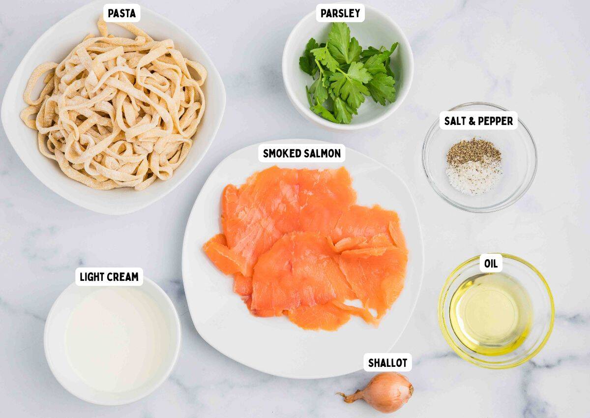 A top-down view of labeled ingredients on a white surface: pasta, smoked salmon, parsley, salt and pepper, oil, light cream, and a shallot. Each item is placed in a separate bowl or plate.