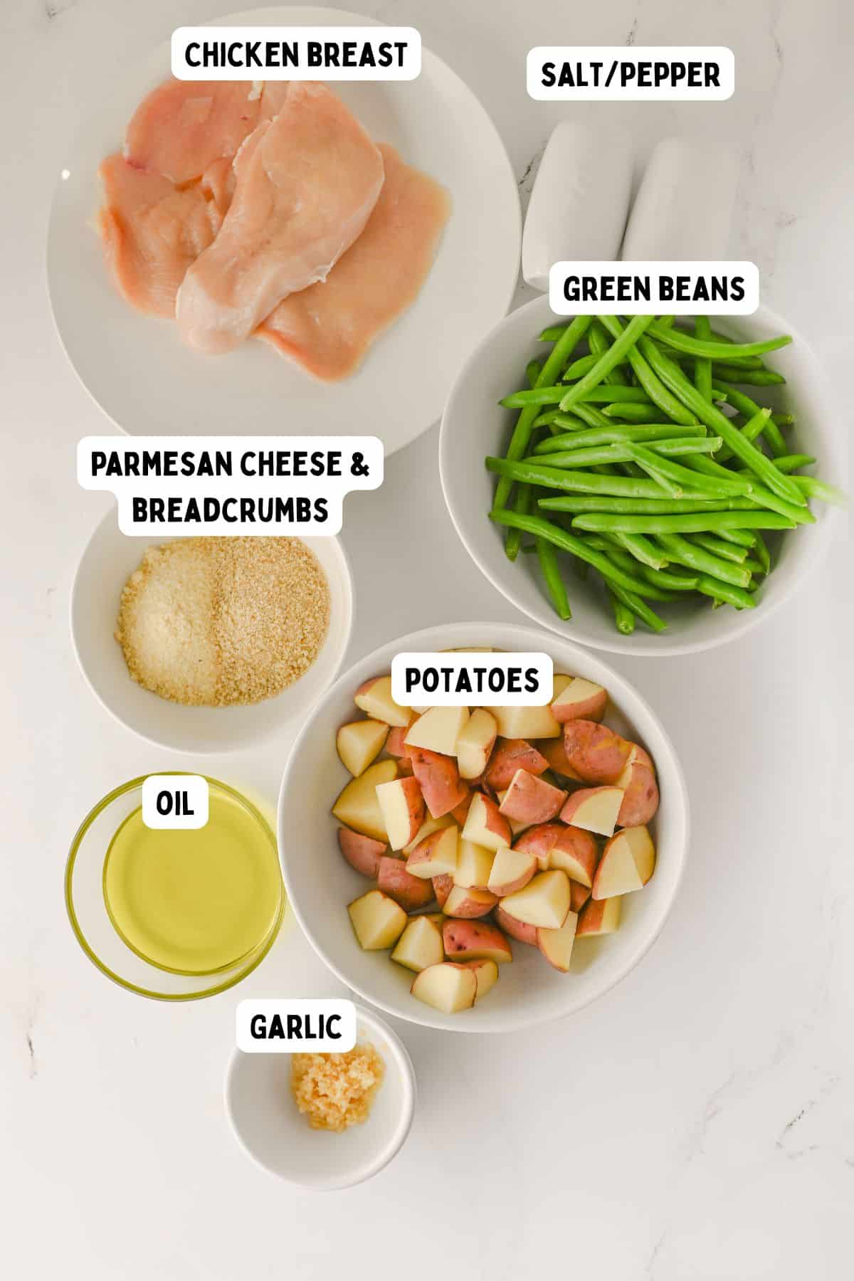 A top-down view of bowls and plates containing raw chicken breast, green beans, chopped potatoes, minced garlic, oil, parmesan cheese and breadcrumbs mixture, and a small bowl of salt and pepper, all labeled.