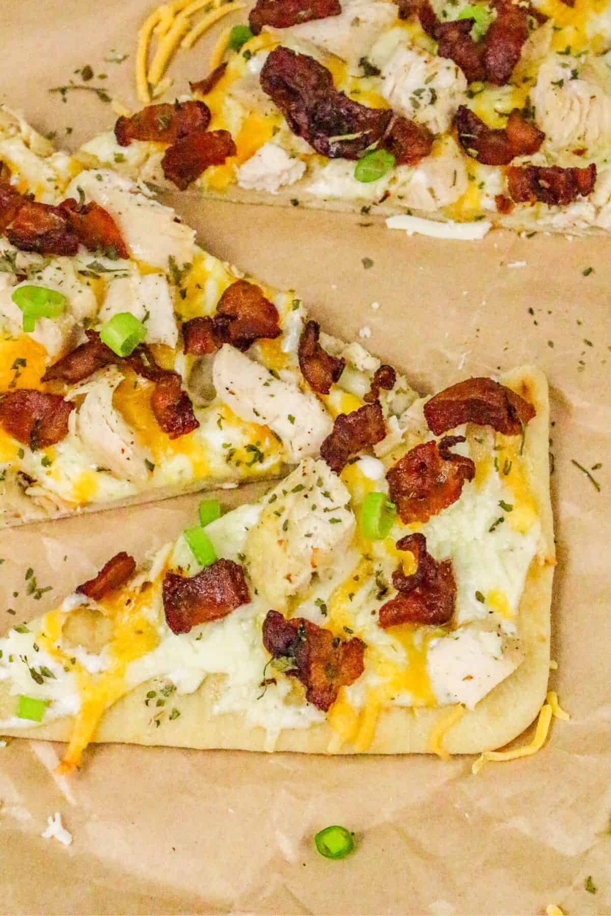 Rectangular slices of chicken bacon ranch pizza topped with cooked chicken, crispy bacon, melted cheese, herbs, and chopped green onions on parchment paper.