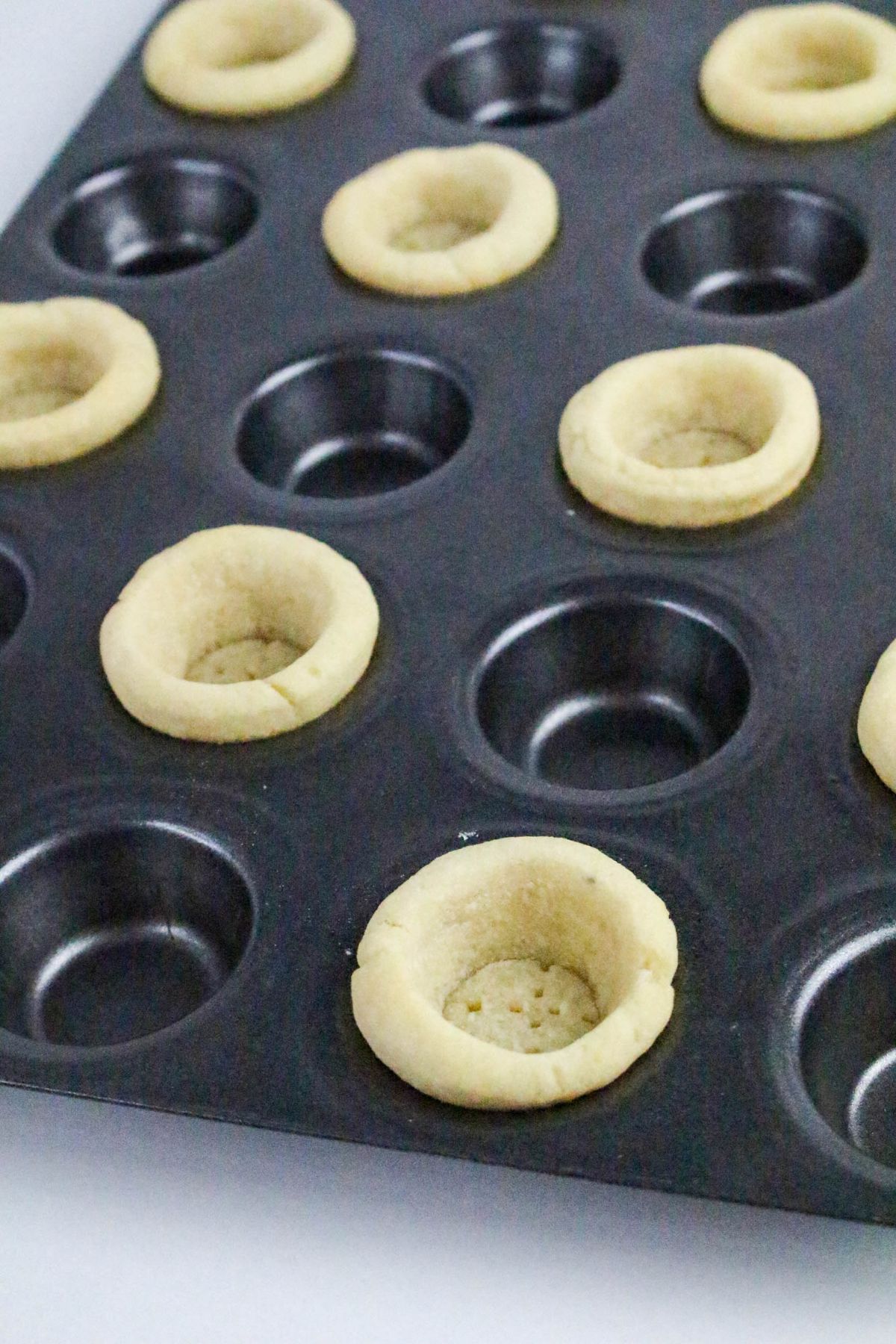 A nonstick muffin tin holds several baked cookie cups, each with a hollow center, while some cups in the tray are empty. The cookie cups are light golden-brown in color.