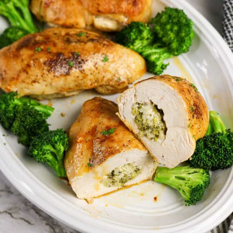 A white plate with chicken and broccoli stuffed chicken breasts, one sliced open to reveal a creamy cheese and green herb filling, garnished with broccoli florets.