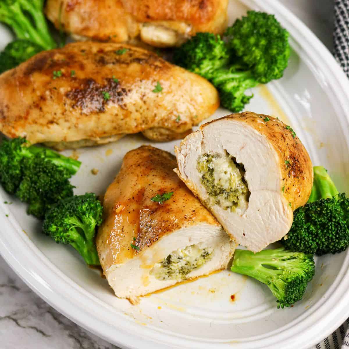 A white plate with chicken and broccoli stuffed chicken breasts, one sliced open to reveal a creamy cheese and green herb filling, garnished with broccoli florets.