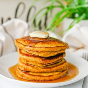 A stack of pancakes topped with a pat of butter and drizzled with syrup on a white plate.