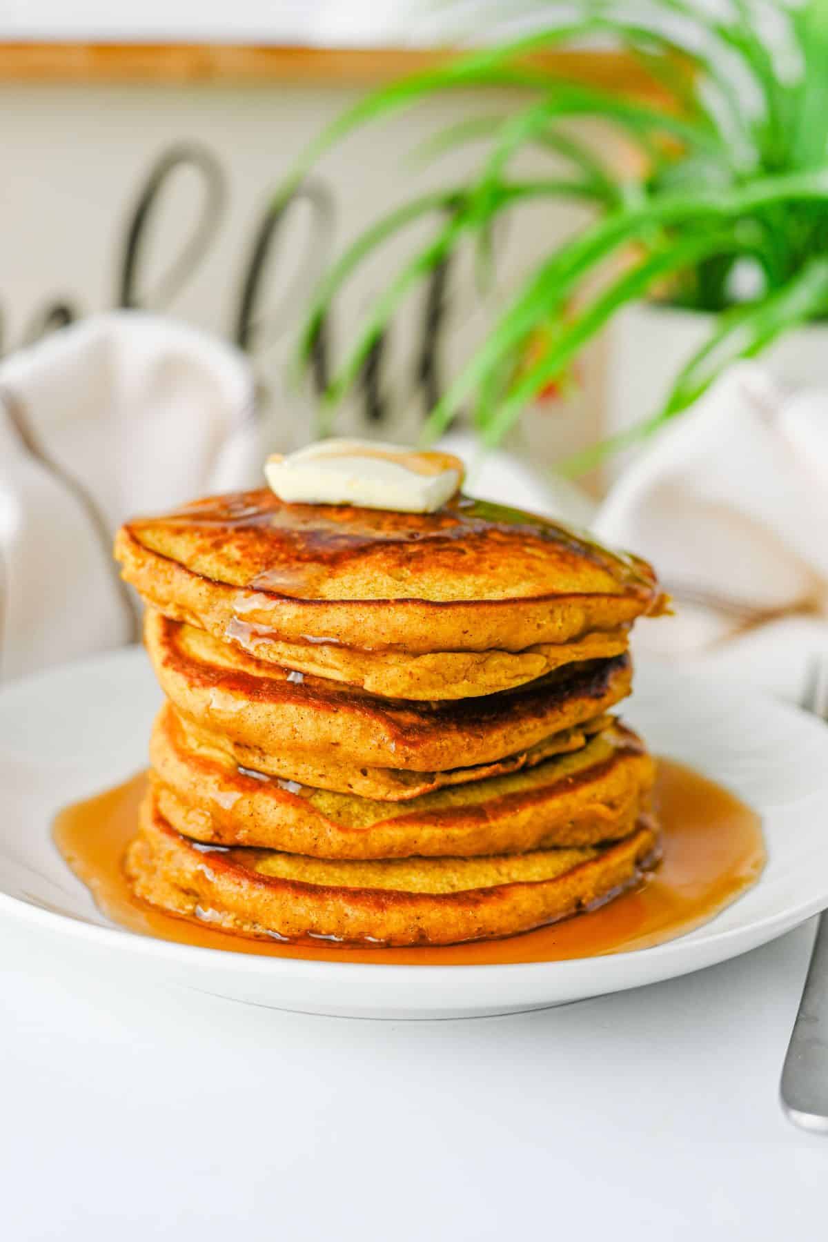 A stack of pancakes topped with a pat of butter and drizzled with syrup on a white plate.