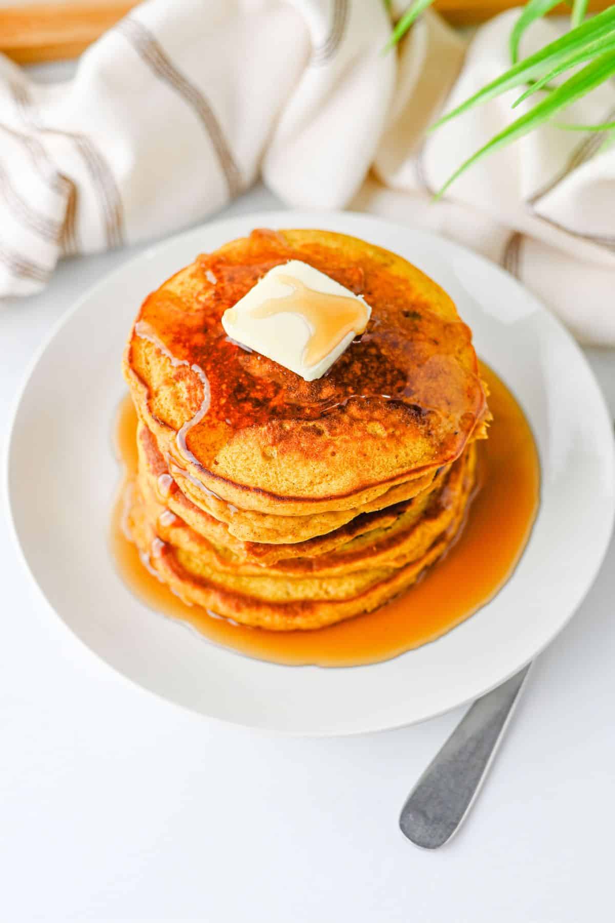 A stack of pancakes topped with a pat of butter and syrup on a white plate.