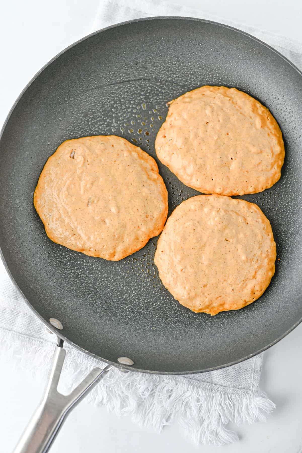 Three pancakes cooking in a nonstick skillet.
